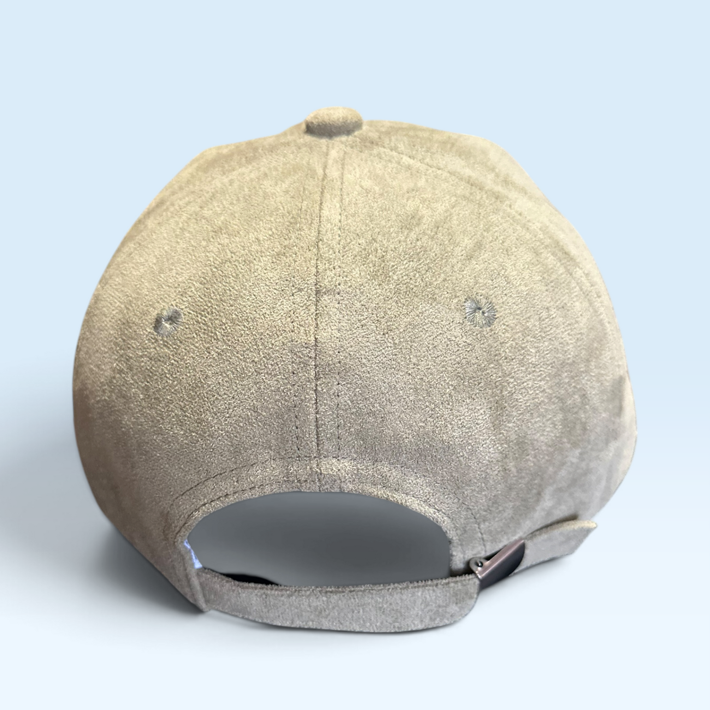 The back view of a light moss green suede baseball cap with an adjustable fabric strap and metal snap closure, set against a light blue background.